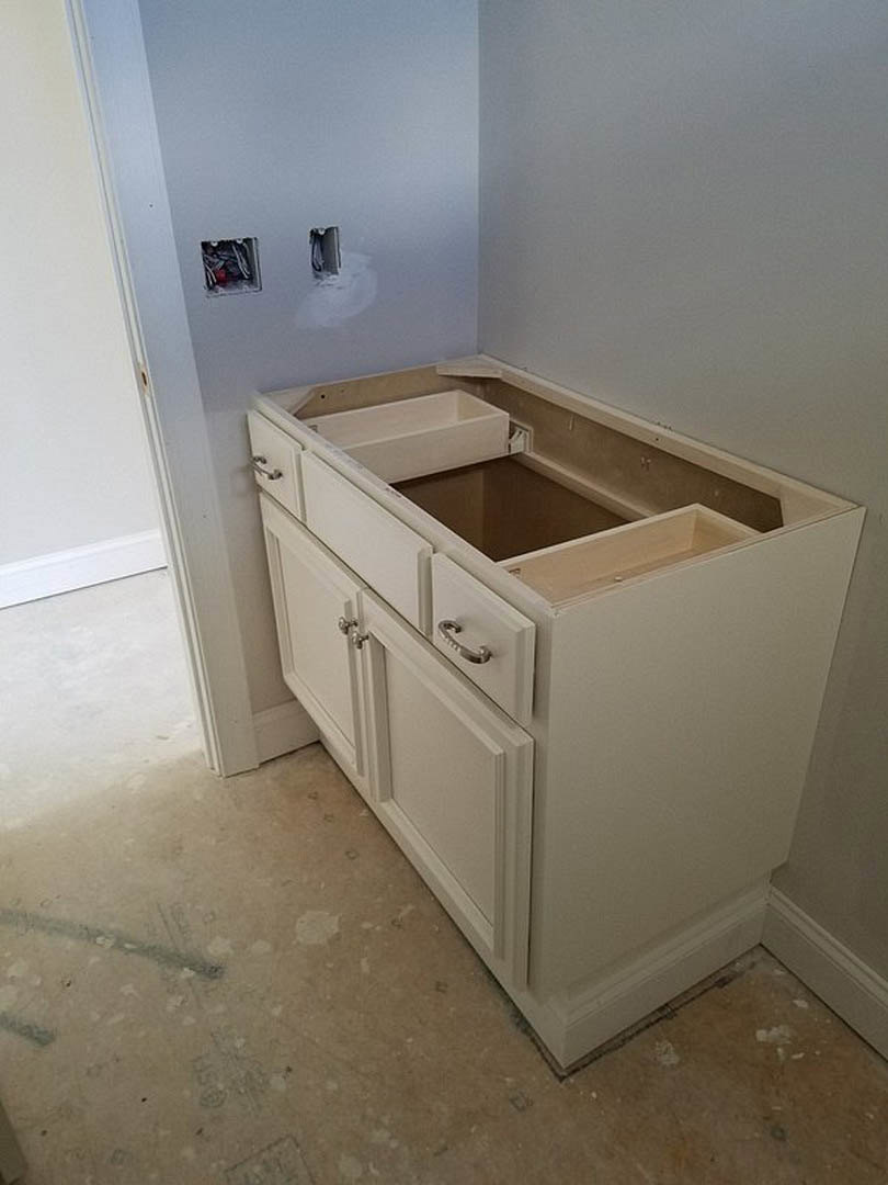 White kitchen cabinet with multiple drawers, quartz countertop, stainless steel sink, light wood flooring, white walls