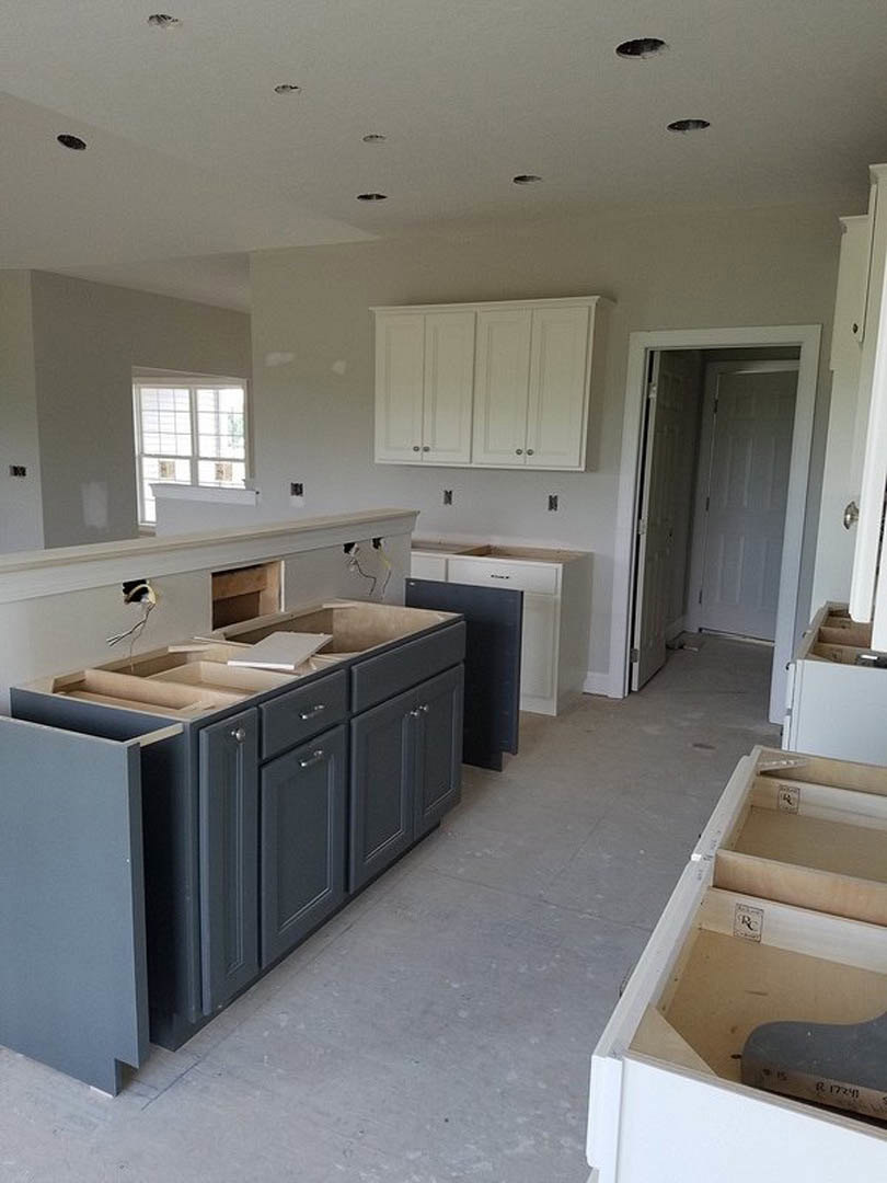 White kitchen cabinets with silver knobs, light stone countertop, stainless steel sink, hardwood flooring, and white walls