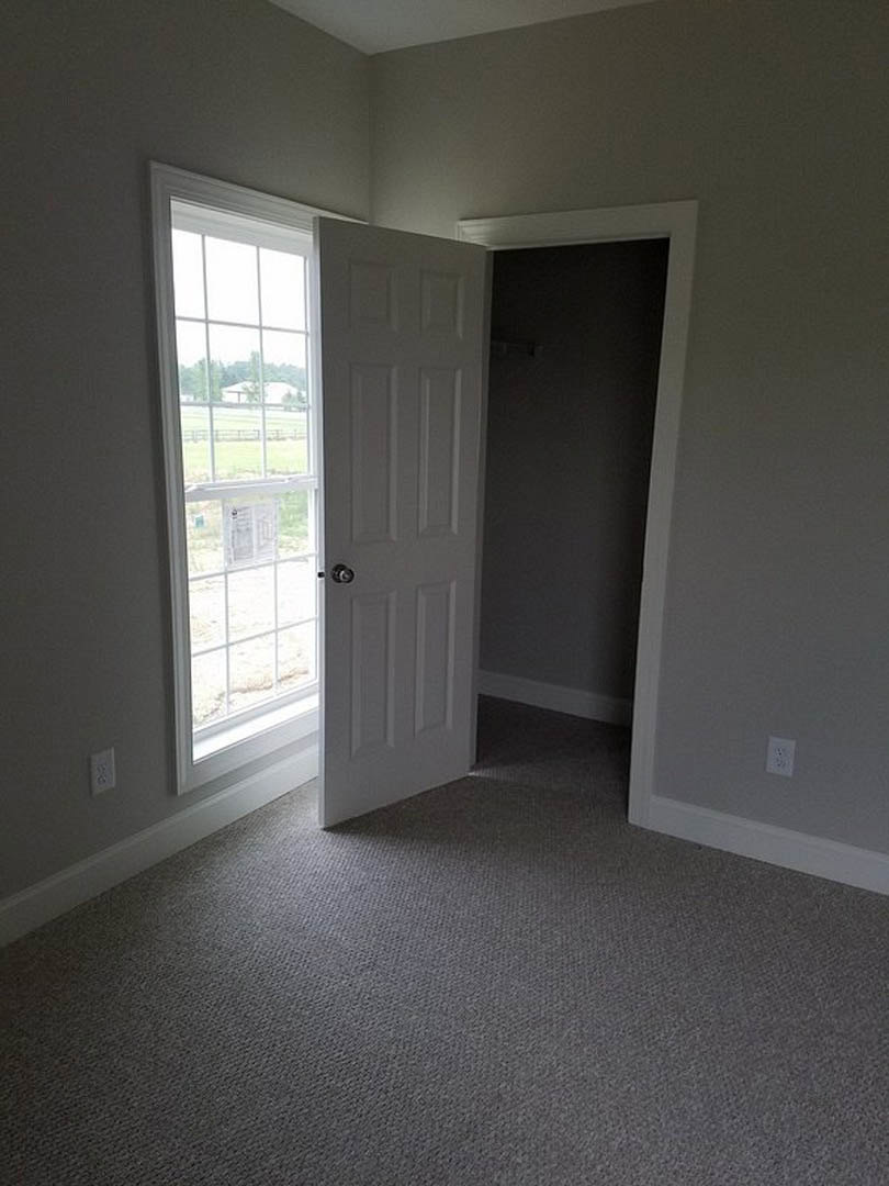 White paneled door open onto carpeted floor, window with newspaper resting on sill, view of fence and grass outside