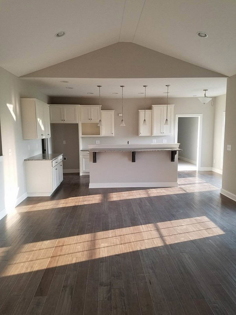 Kitchen with white countertops, wood flooring illuminated by sunlight, bar seating, white walls, and decorative bowl on counter