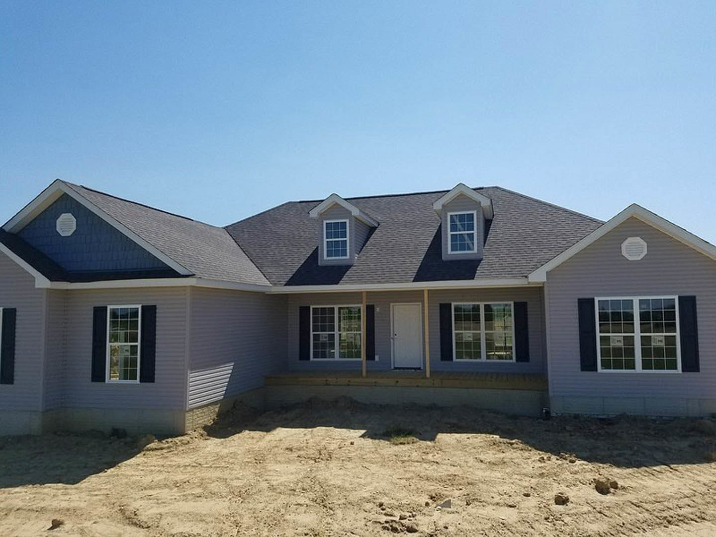 Partially built house with exposed dirt yard, covered front porch, white door featuring black handle, white vent with black lines, octagonal architectural detail, and close-up of