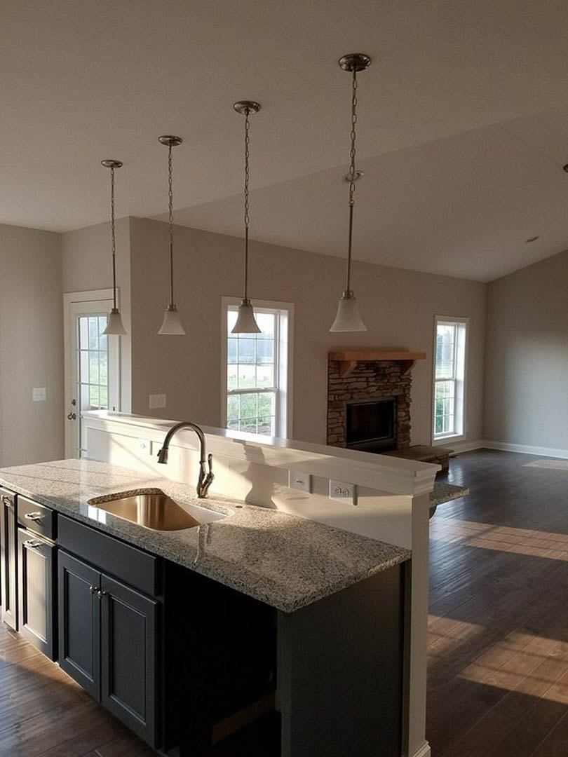 Granite countertop kitchen with undermount sink, tile backsplash, white cabinetry, built-in fireplace with black frame, pendant lamp with white shade, and metal chain hanging from