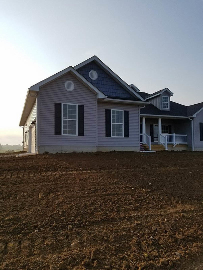 Two-story house with blue roof, multi-pane windows, white porch railing, and expansive grassy front yard