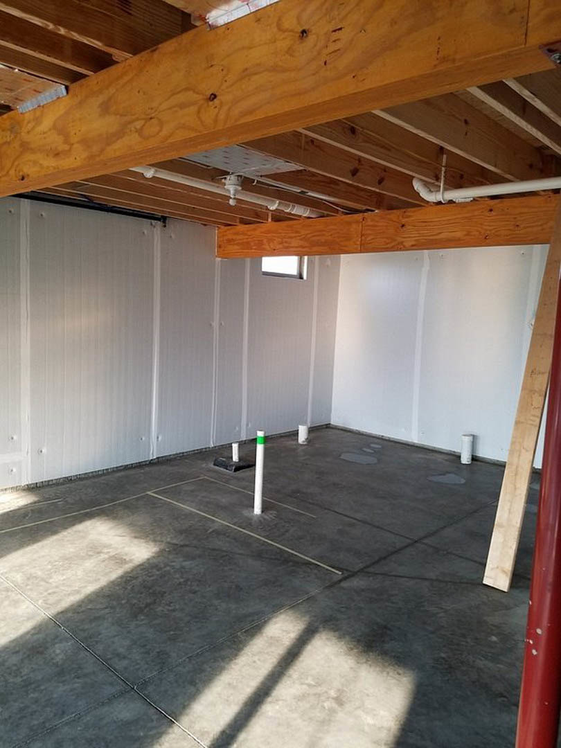 White walls with vertical lines, exposed wooden ceiling beams with holes, concrete floor featuring white support poles, window shadow cast across the floor, close-up of a white