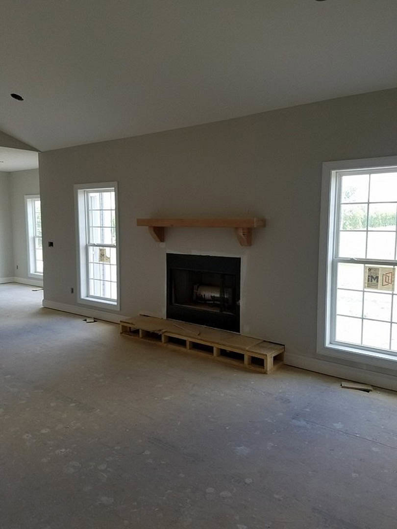 Living room with plaster walls, wood flooring, white-framed windows, and a built-in fireplace surrounded by wooden beams