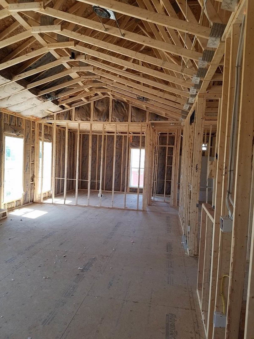 Exposed wood ceiling beams, white-framed window, unfinished walls, construction materials on floor
