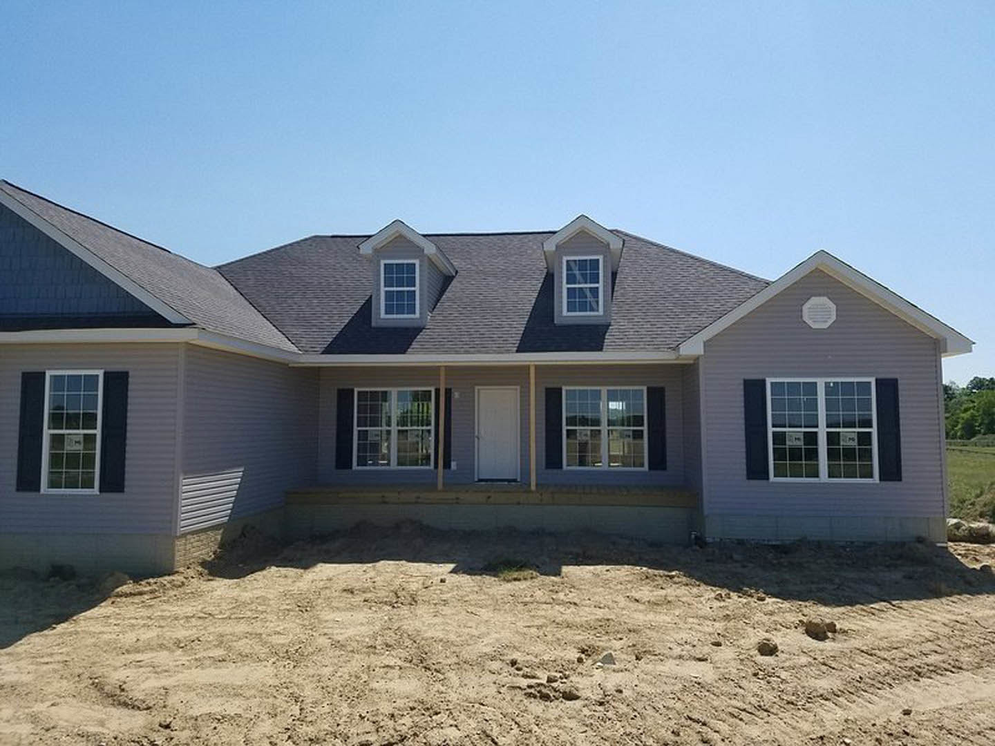 Two-story house under construction with exposed dirt yard, white siding, covered porch, white front door, and multiple windows