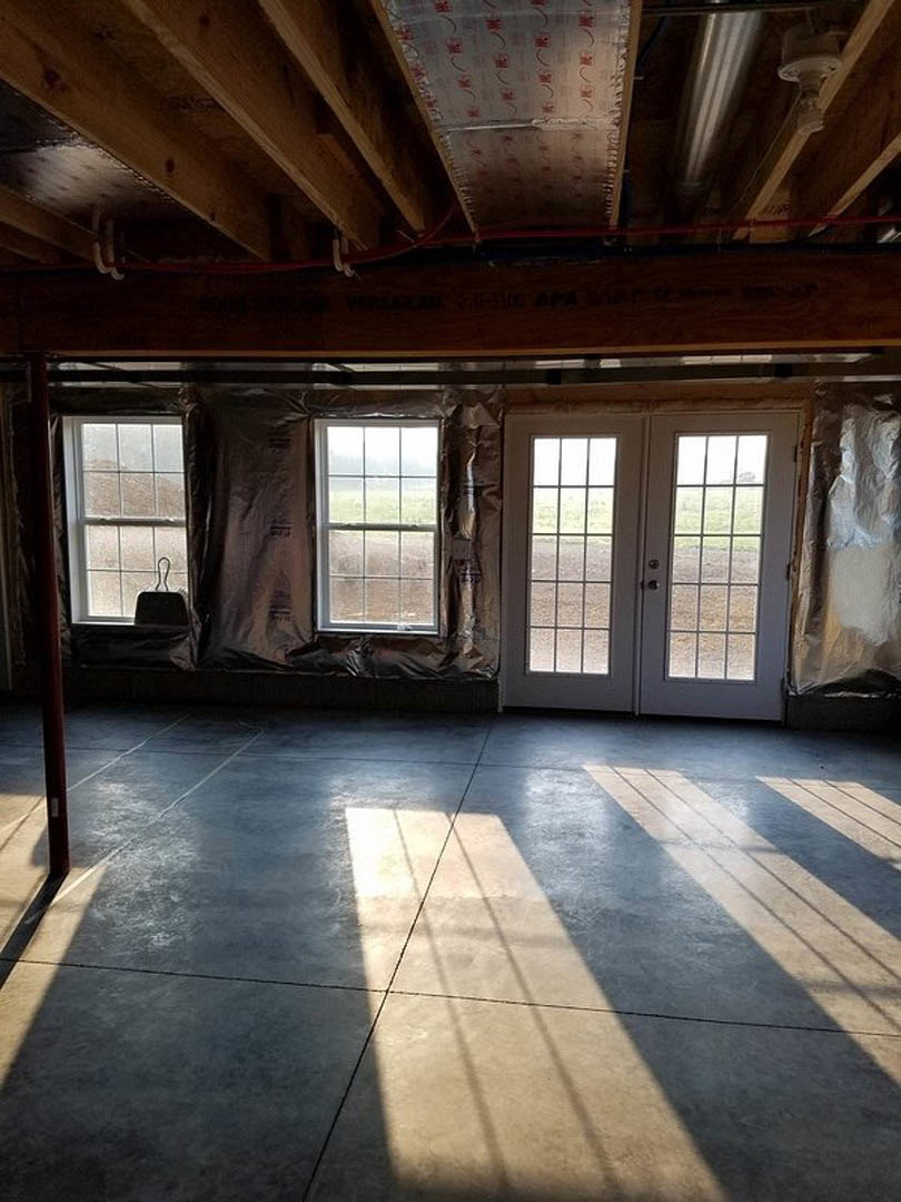 Wood plank ceiling with exposed beams, large windows and double glass-paneled doors, concrete floor illuminated by natural light, view of grassy yard outside
