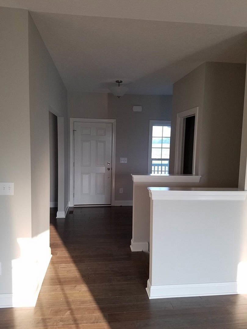 Hallway with laminate flooring, white walls, white door with silver trim, wooden baseboard, window overlooking water, and visible light switch