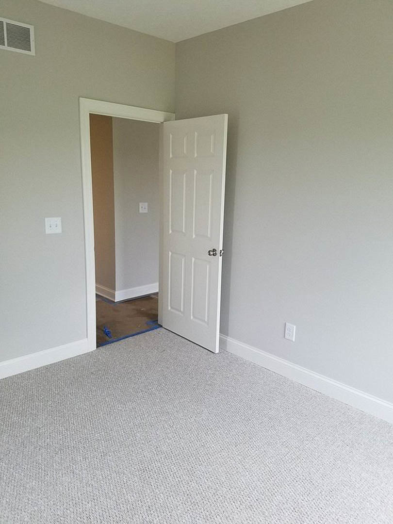 White paneled door opening to a carpeted room with light-colored walls, floor vent, and decorative molding