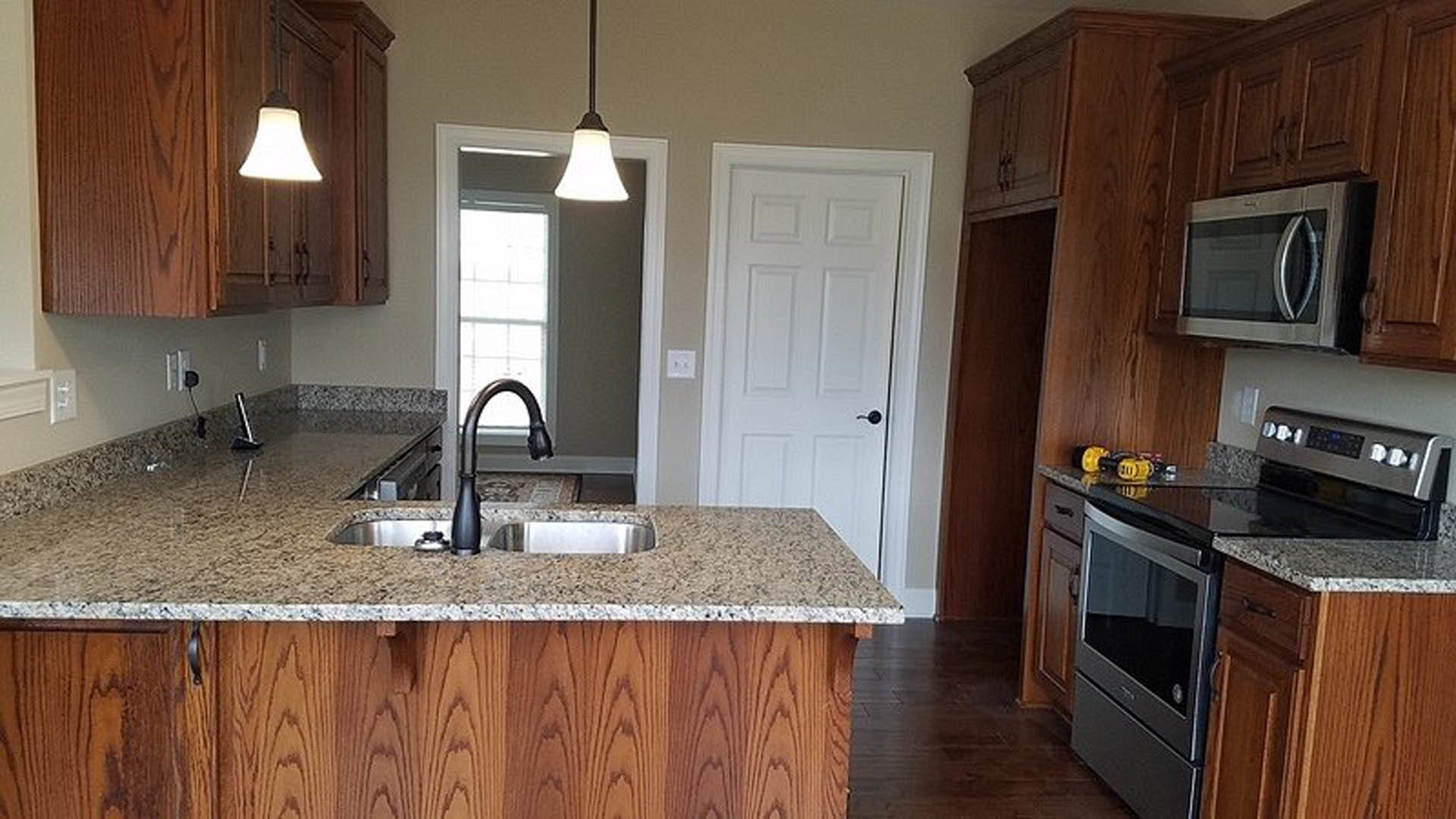 Granite countertops, white cabinetry, stainless steel stove and microwave, neutral backsplash in a modern kitchen