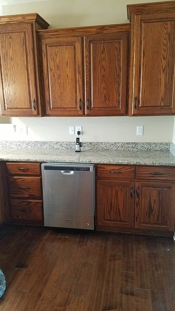Granite countertop kitchen with white cabinetry, stainless steel dishwasher featuring a black handle, and upper cupboards against a neutral wall
