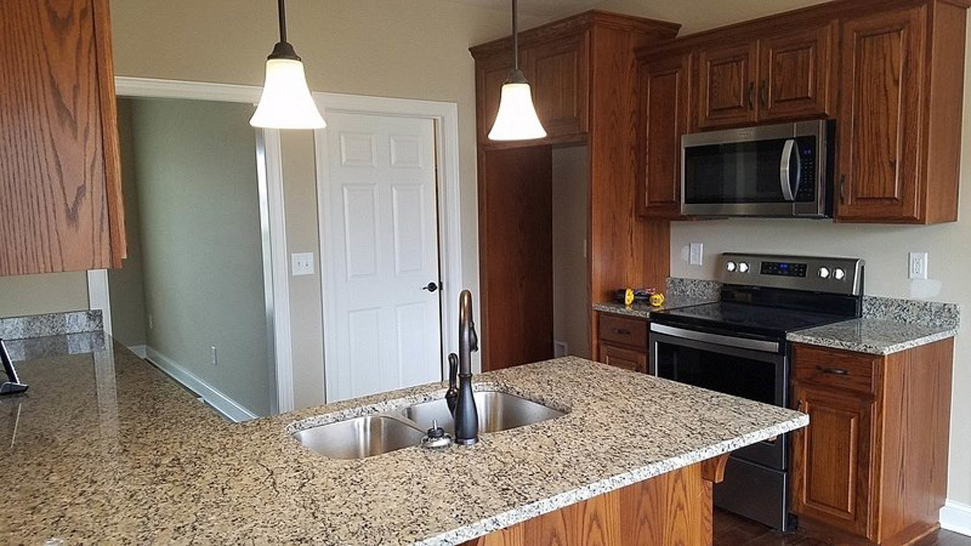 Granite countertops, white cabinetry, stainless steel microwave, undermount sink, silver faucet, white wall with double black-knob light switch