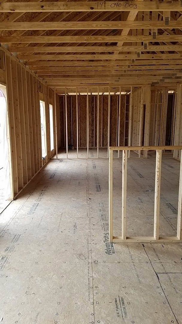 Exposed wood framing with beams and planks on ceiling and floor in unfinished residential interior