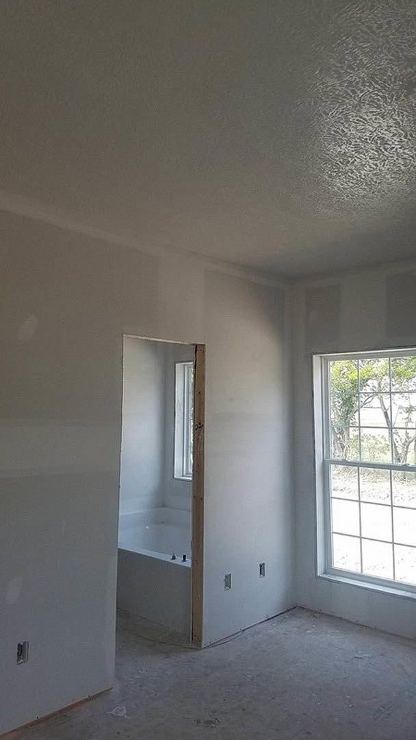 Freestanding white bathtub beneath a large window, light plaster walls, wood door, natural daylight filling bathroom