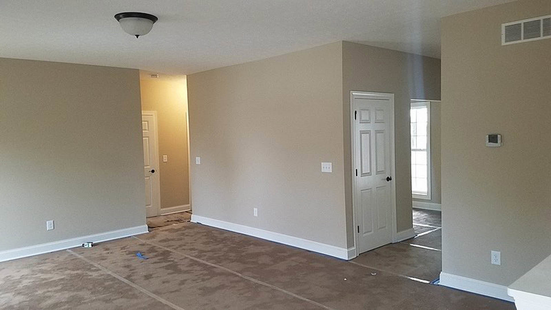 Carpeted room with light-colored plaster walls, white door, and tile flooring visible near entry