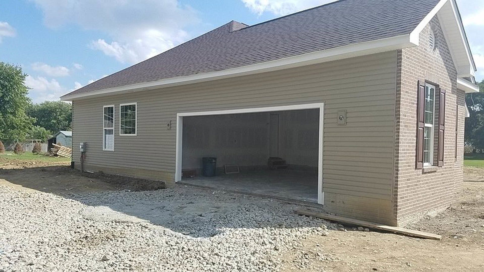 White paneled garage door with windows, open to reveal interior; gray siding exterior, concrete driveway, trash can near entrance, wooden pallet and black object inside garage