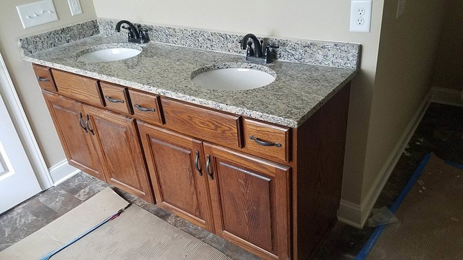 Granite countertop with undermount bathroom sink, chrome faucet, white cabinetry, and tiled backsplash