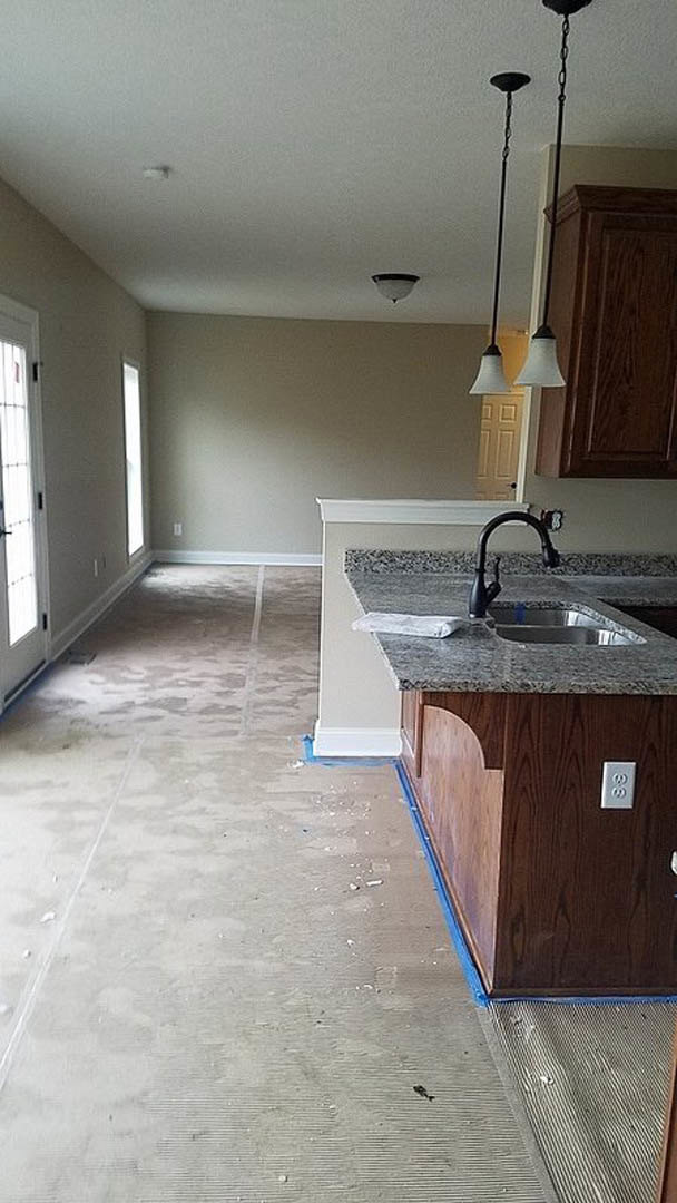 Modern kitchen featuring two sinks, one set into a central island and another along the tiled backsplash, with white cabinetry, stone countertops, and hardwood flooring.