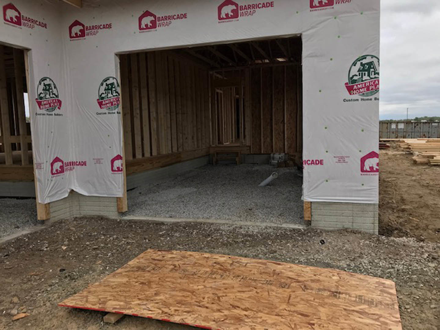 White exterior wall under construction with exposed plywood, temporary white sheet, and a white sign featuring red text and bear logo; unfinished wooden planks visible near ground