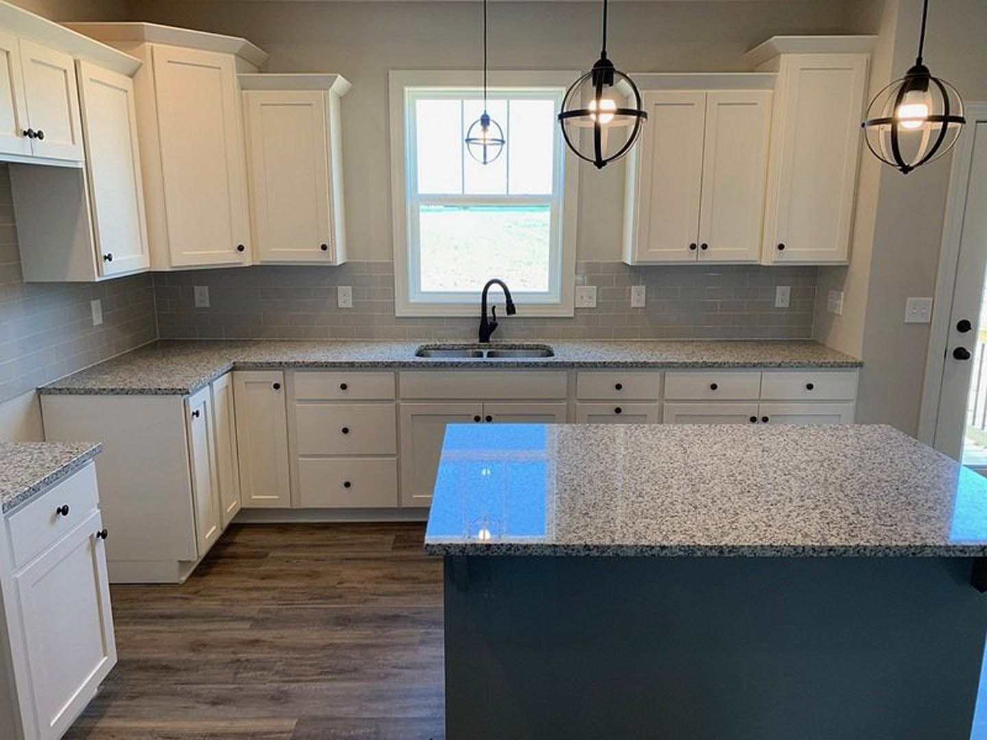 White kitchen cabinets and granite countertops, stainless steel faucet, round glass globe ceiling light, neutral walls, built-in appliances, and under-cabinet lighting.