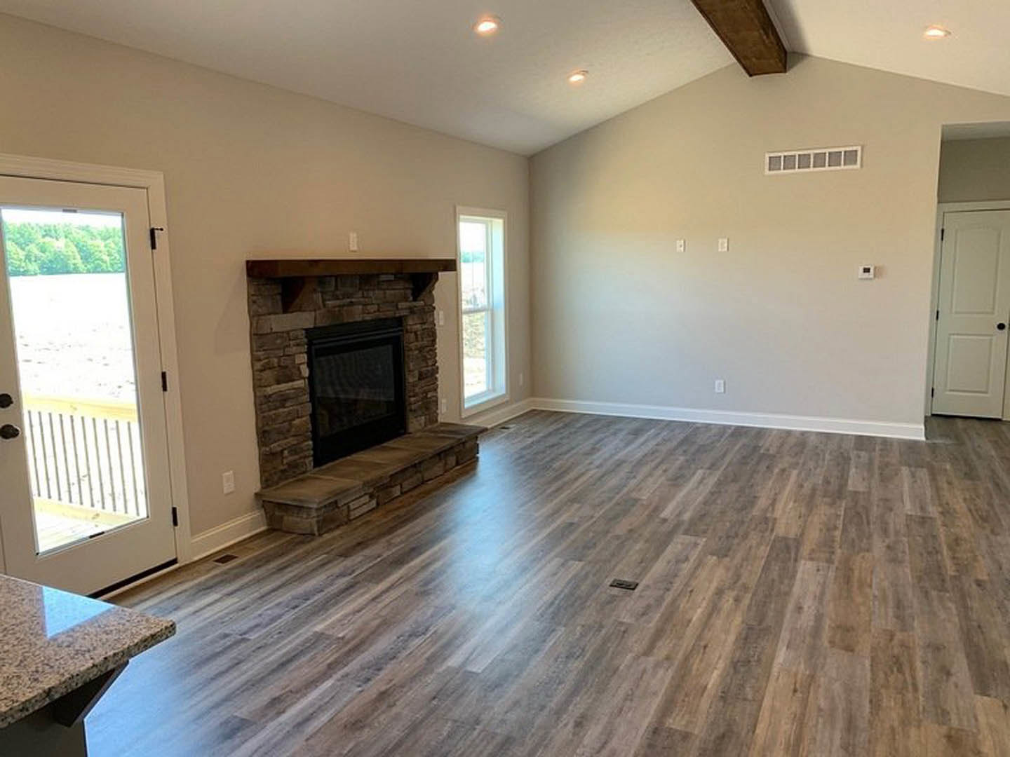 Living room featuring hardwood floors, white walls, a central fireplace with stone surround, and adjacent white doors with black hardware