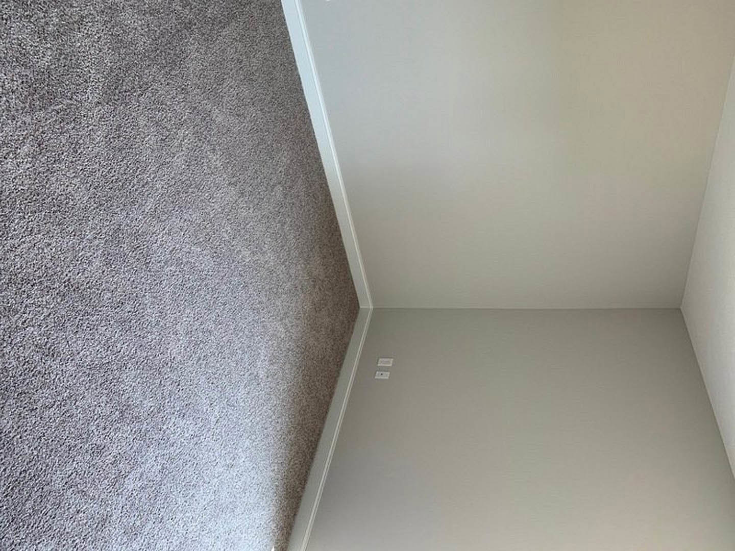 Carpeted room with white plaster walls, white door, and rectangular wall-mounted object; grey granite surface with black stripe visible.