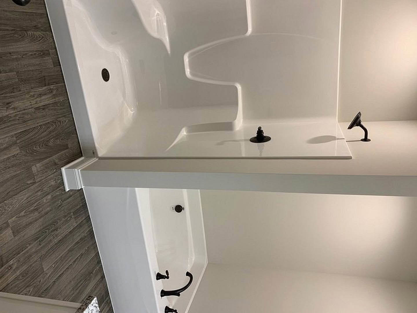 Freestanding white bathtub with matte black faucet and fixtures, wood plank flooring, white baseboard, neutral bathroom walls