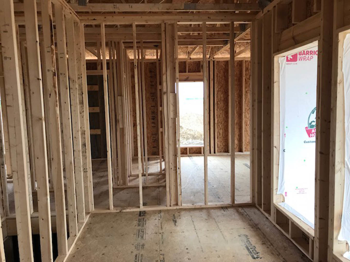 Wood-framed room under construction with exposed beams, unfinished floor, window revealing snowy landscape, and a white sign with red and green text.