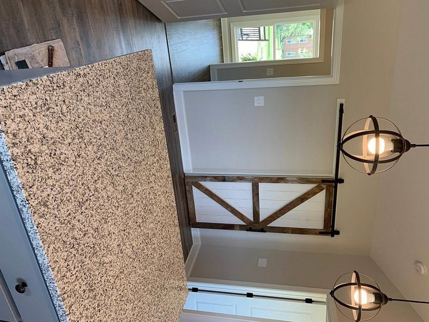 Modern kitchen with white cabinetry, stainless steel sink, stone countertop, and a circular metal light fixture suspended above.