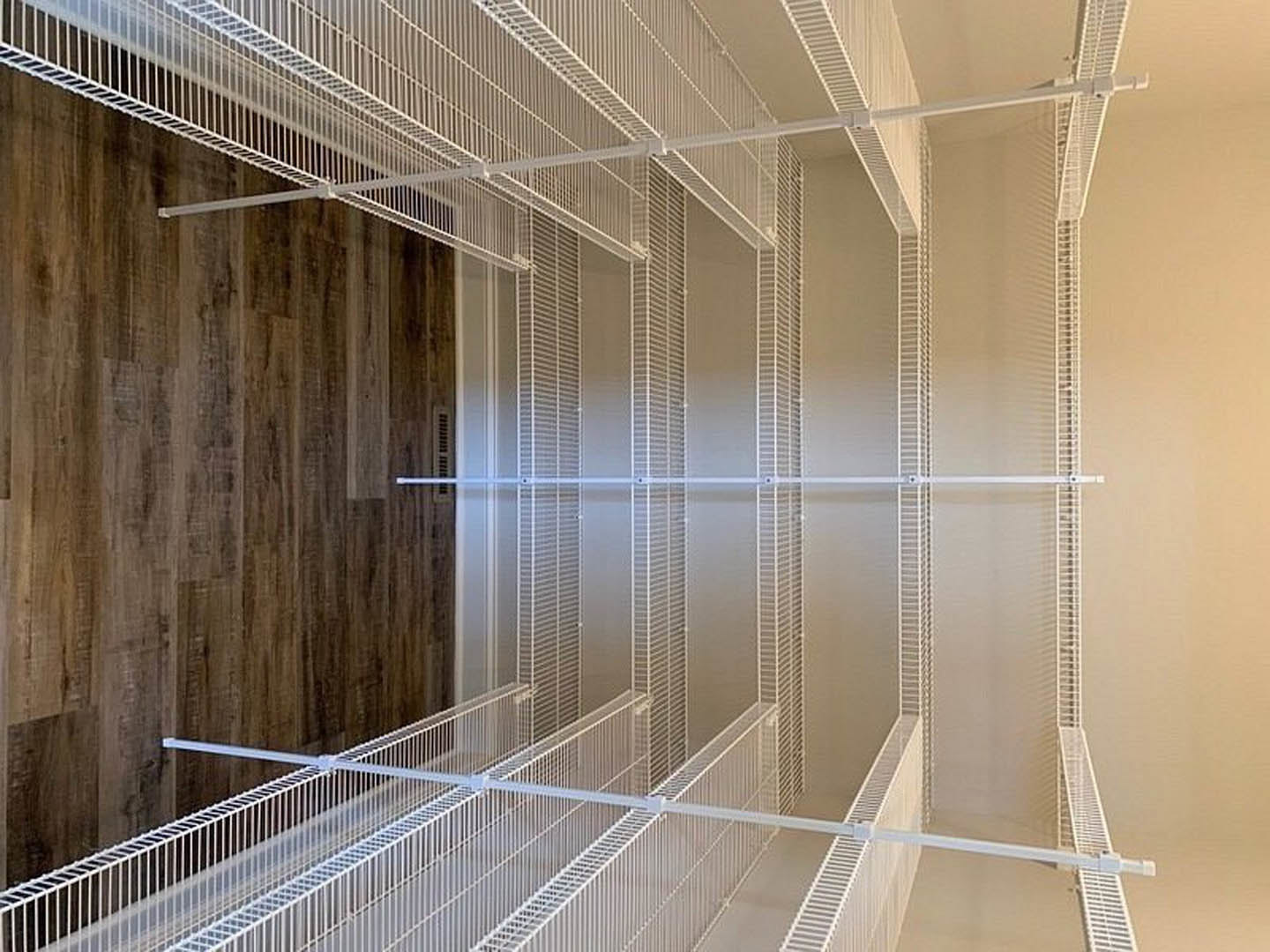 Wood floored room with built-in white shelves, wood paneled wall featuring a metal handle, and white metal grate mounted on wall