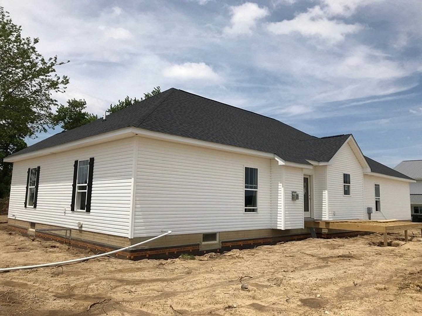 White house under construction with black roof, white-framed window, wooden planks on ground, blue sky overhead