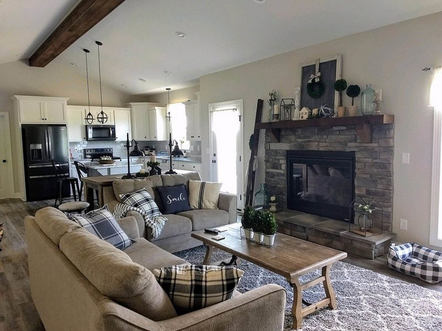 Living room with stone fireplace, two upholstered couches with pillows and blanket, wooden coffee table holding a potted plant, light-colored walls, hardwood floor, and ceiling