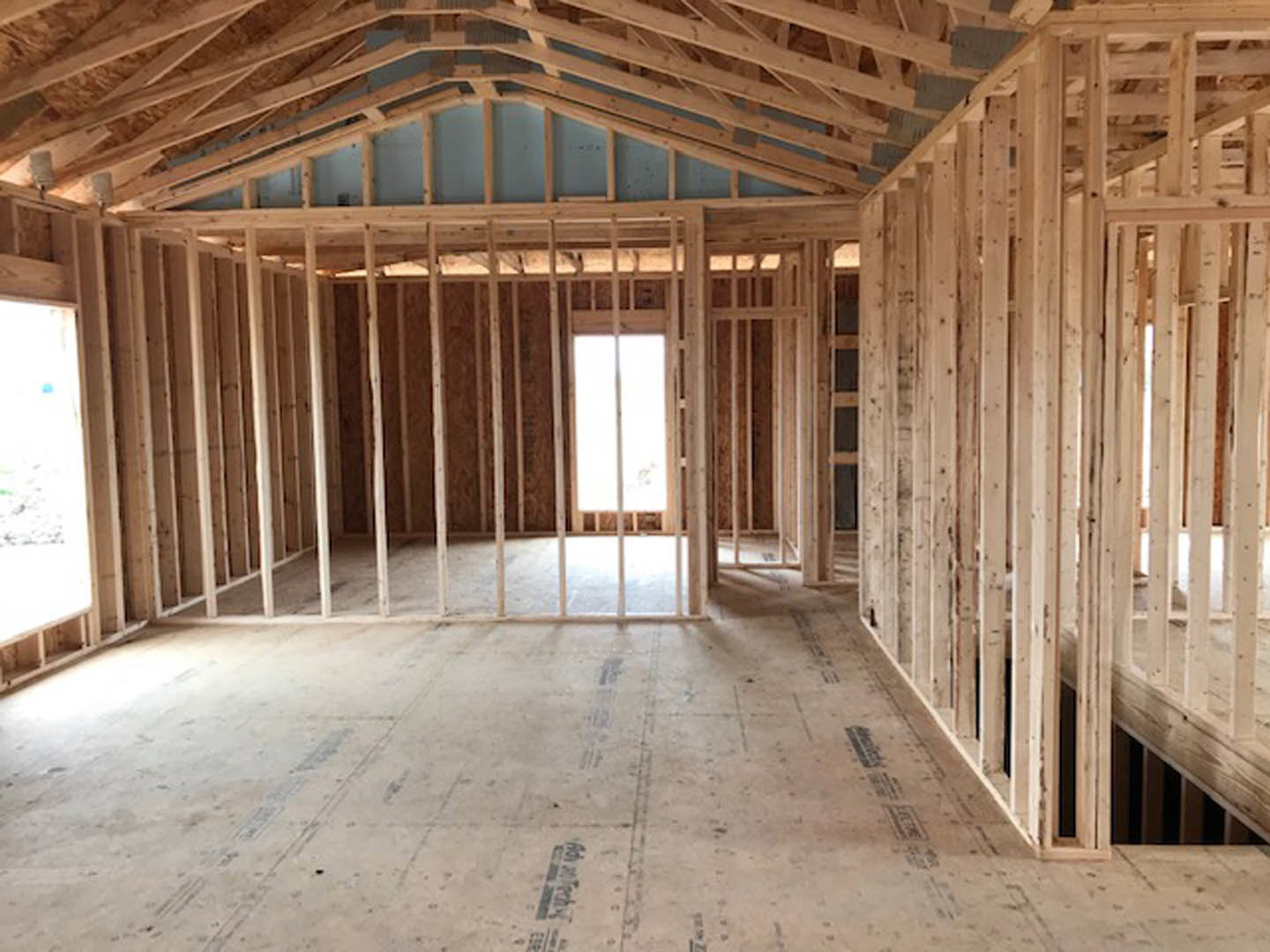 Wood-framed room under construction with exposed beams, concrete floor, white boards, and window