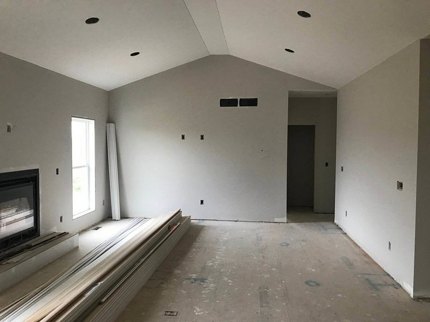 Spacious room with multiple floor levels, white rectangular window letting in natural light, plaster walls, wood stack near wall, dirty spotted flooring, close-up of curtain and