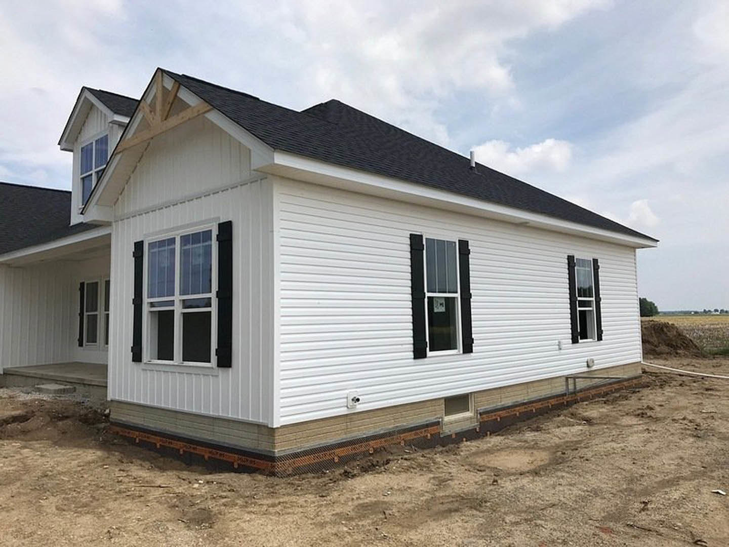White siding house under construction with exposed foundation, metal mesh reinforcement, and window displaying a permit sign; cloudy sky overhead