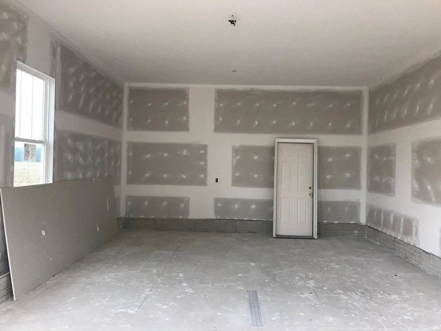 White paneled door with silver handle set in a plaster wall, concrete floor, white-framed window, and minimal modern finishes