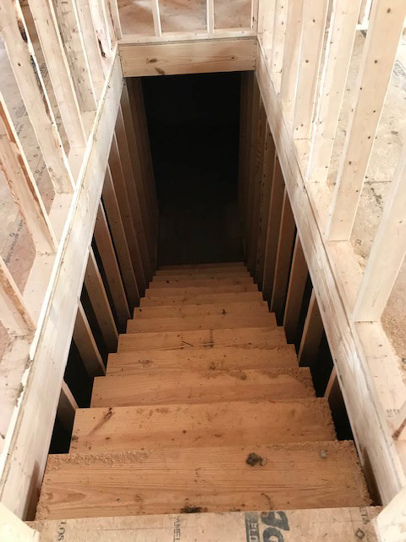 Wooden staircase with plank steps leading down to a basement, surrounded by neutral walls and dim lighting