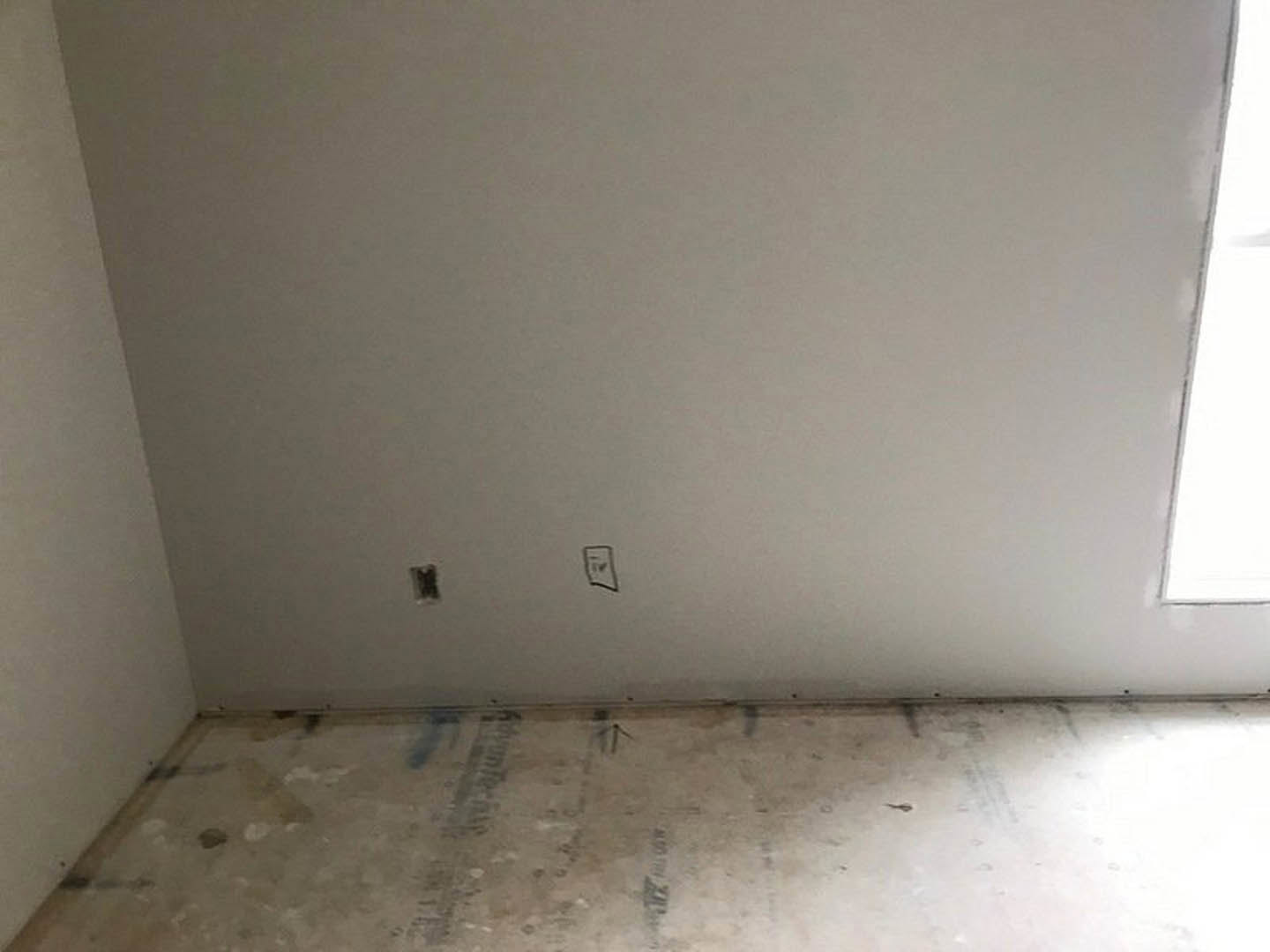 White-walled room with smooth white flooring, black abstract drawing on wall, small holes visible in plaster, minimal furnishings