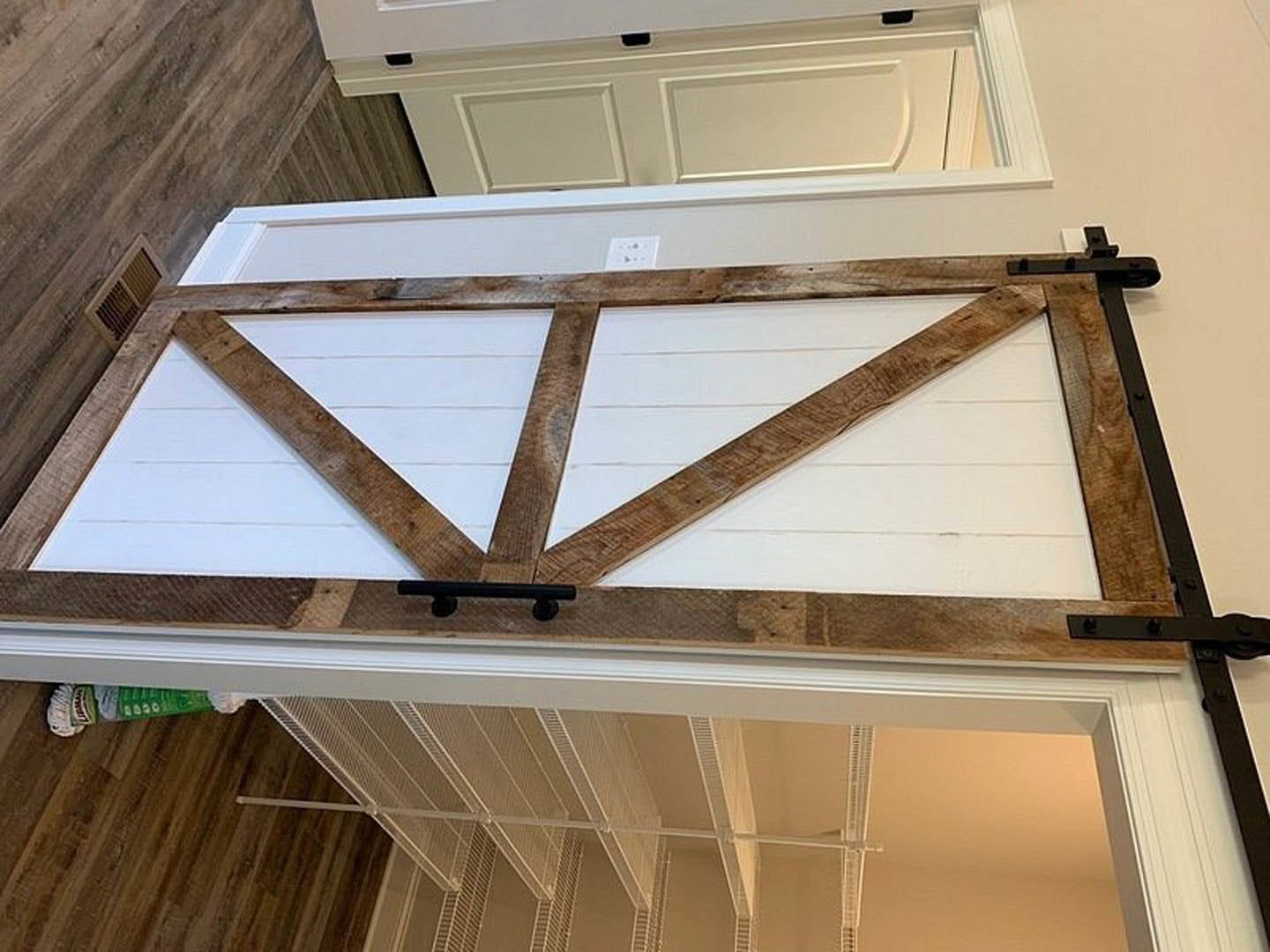 White door with natural wood frame, vertical wood plank wall, black metal bar on light hardwood floor, green box with white circles in foreground