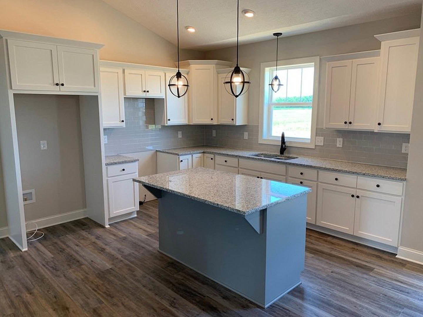 Kitchen with wood flooring, central island featuring marble countertop, white cabinetry with black handles, upper cabinets above wall, window allowing natural light, white square
