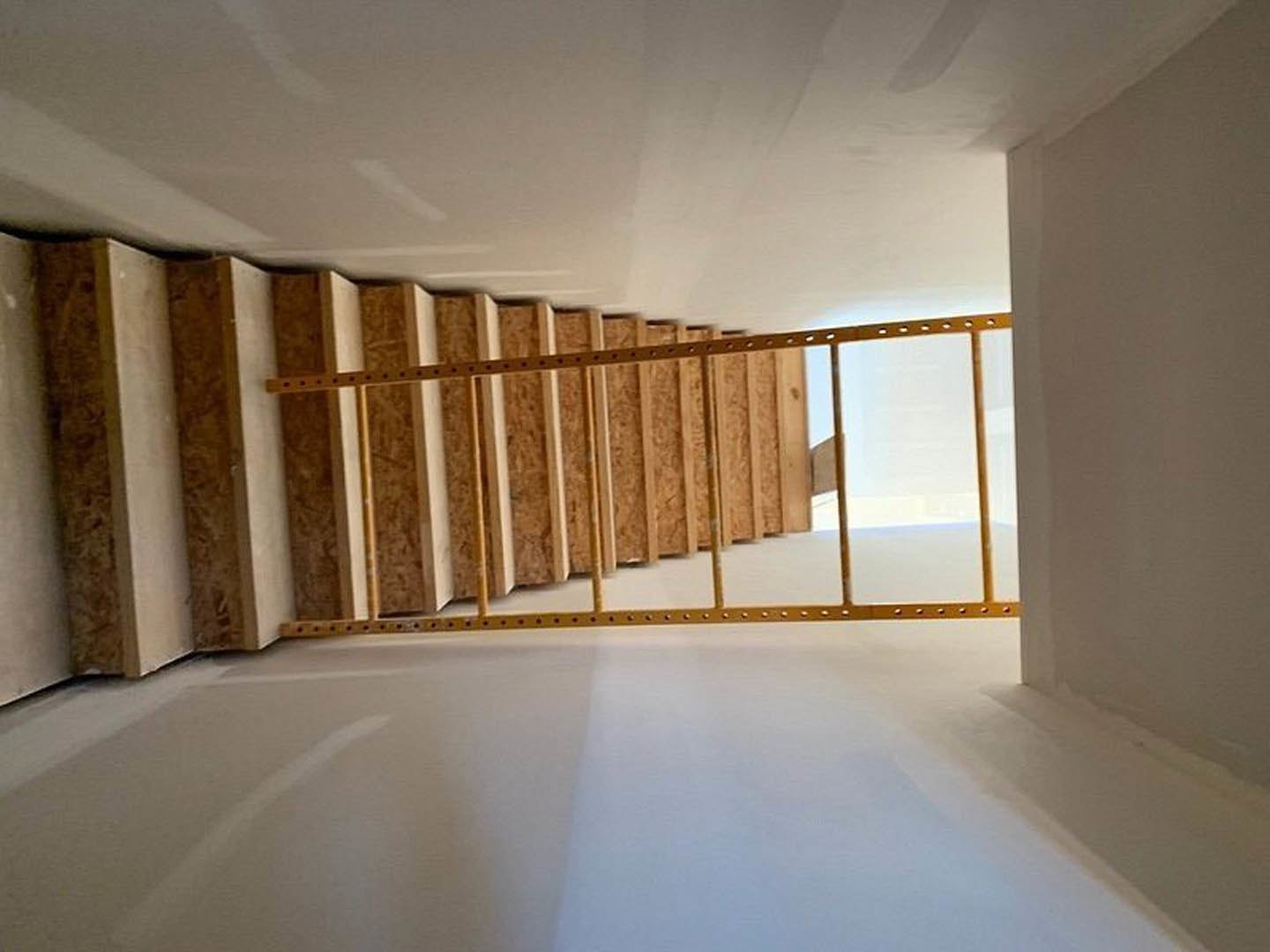 Wooden staircase with black metal frame and ladder, white plaster walls, light hardwood flooring, gold accent frame
