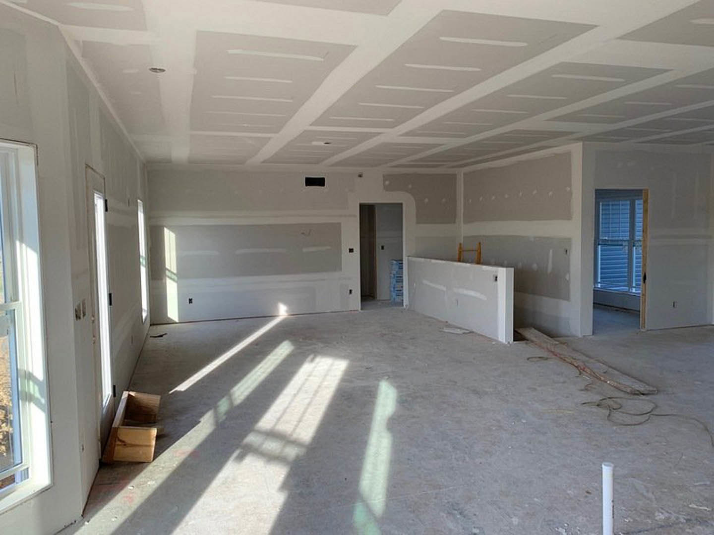 Bright room featuring a white plaster wall, large windows with blinds, light wood flooring, and recessed ceiling fixtures.