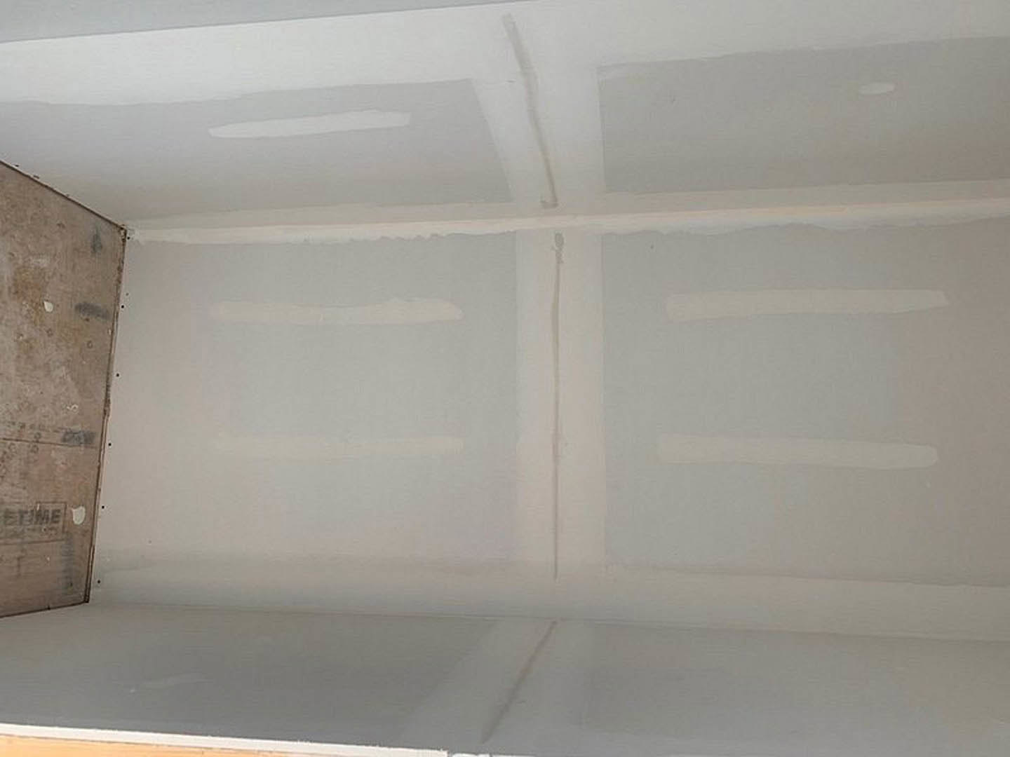 White ceiling and walls with smooth plaster finish, light-colored floor, geometric white and black ceiling accents, minimal modern interior.