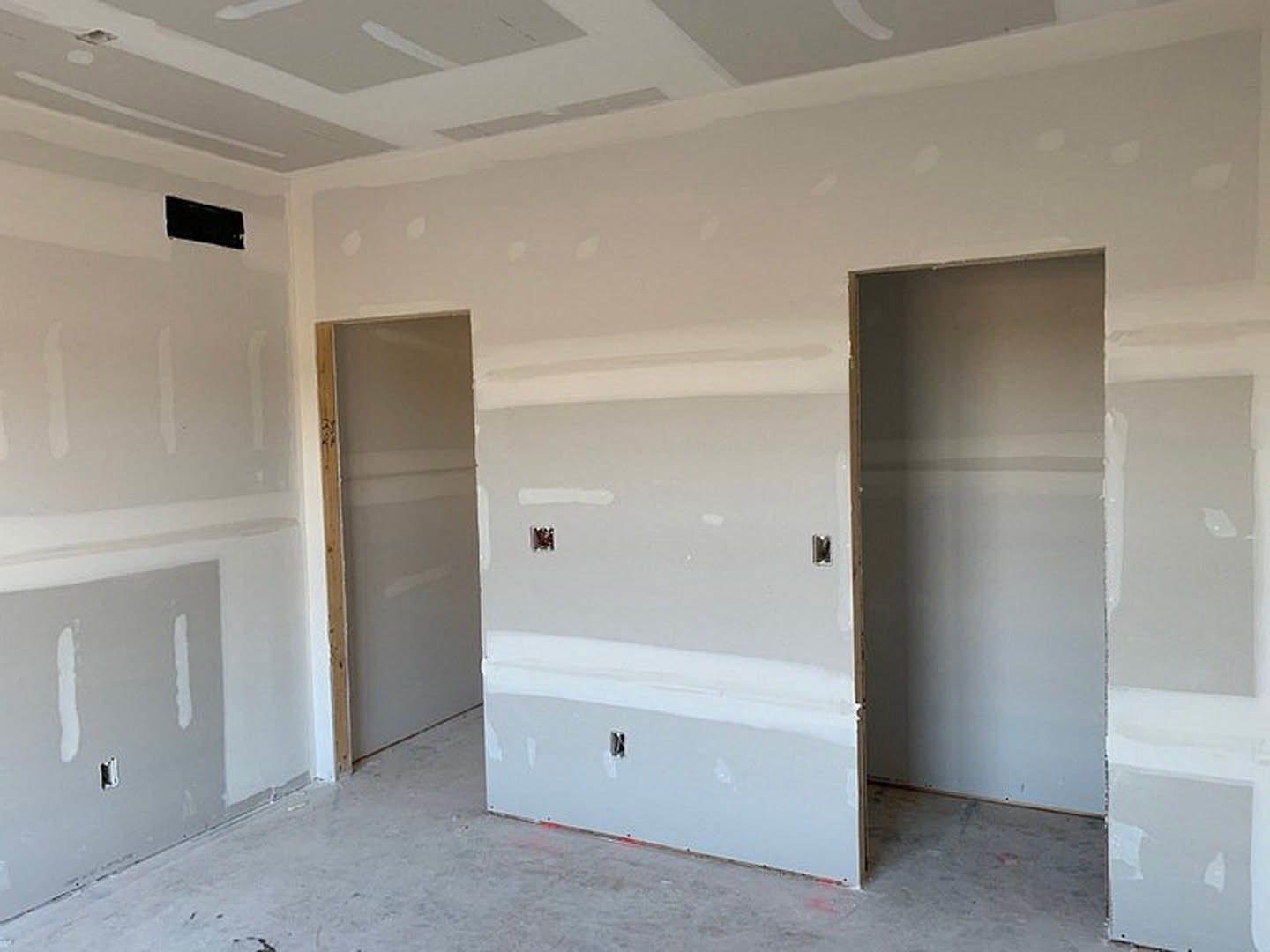 White-painted walls, wooden door frame, white door, light-colored flooring, black rectangular object mounted on wall, plaster ceiling