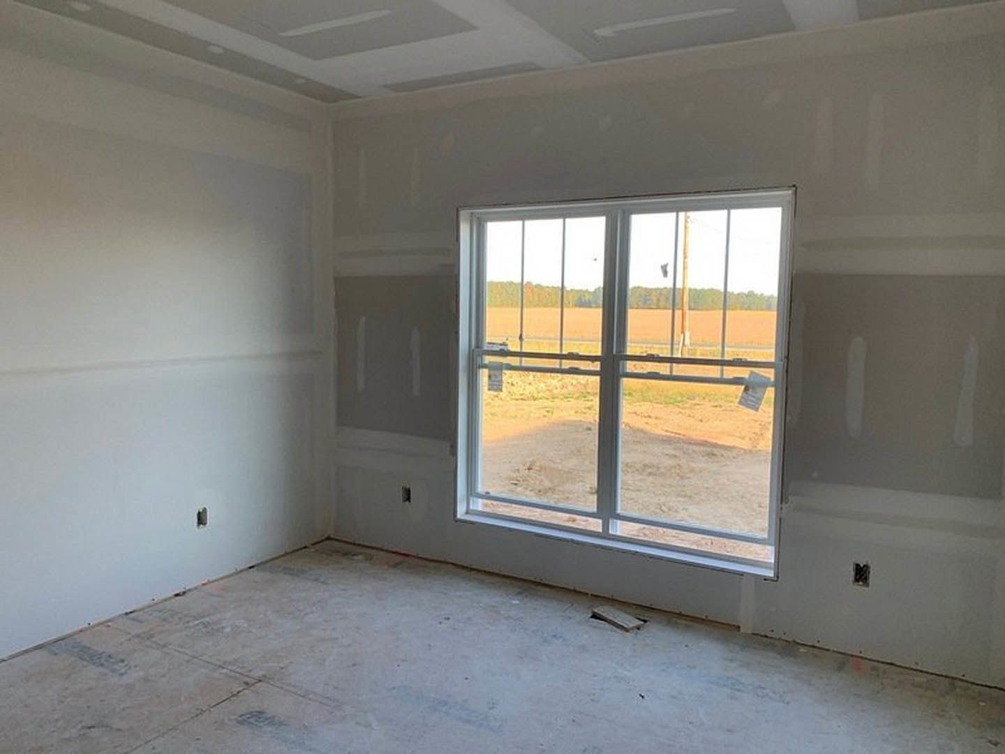 Sunlit room with plaster walls, large window overlooking grassy field, hardwood flooring