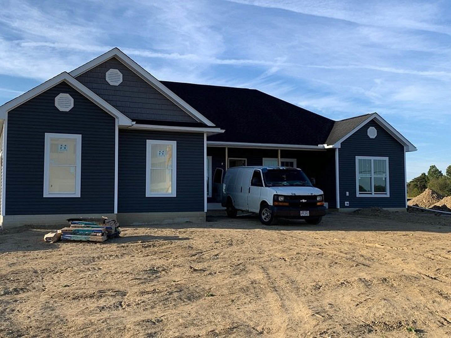 Two-story custom home with dark siding, white trim, and large windows; white van parked on driveway in front of garage; overcast sky above