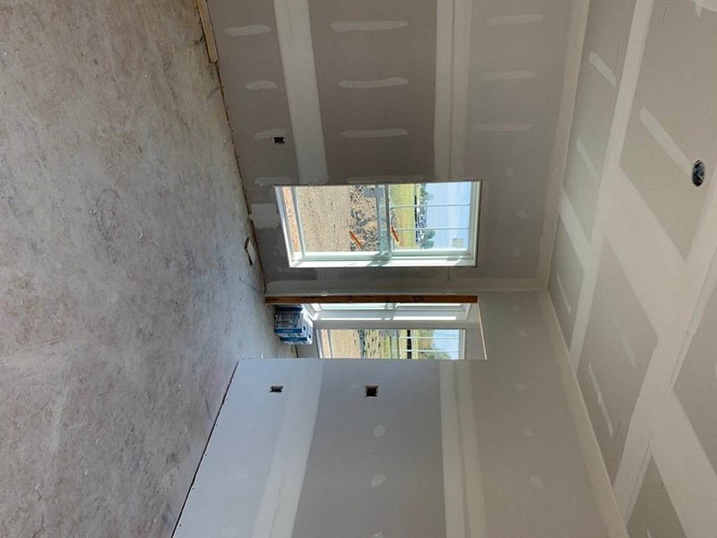 White plaster bathroom with large window overlooking grassy field, smooth white floor, recessed wall niche, and ceiling daylighting.