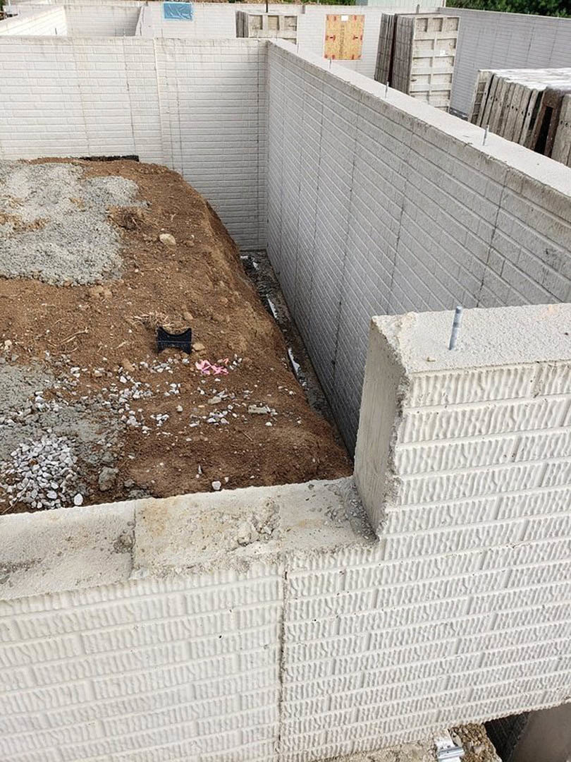 Concrete foundation surrounded by dirt and rocks, unfinished exterior construction with exposed cement and gravel