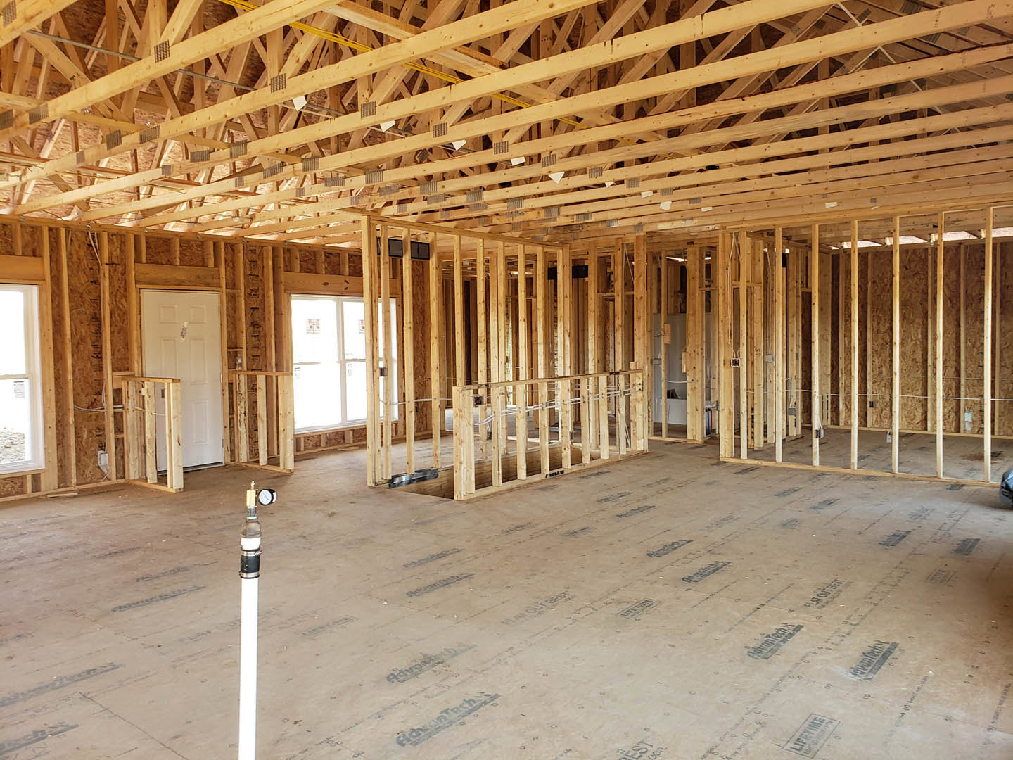 Exposed wood ceiling beams, unfinished wood floor framing, white support pole on concrete, white door with wooden railing, white utility box with label, yellow tape marking on